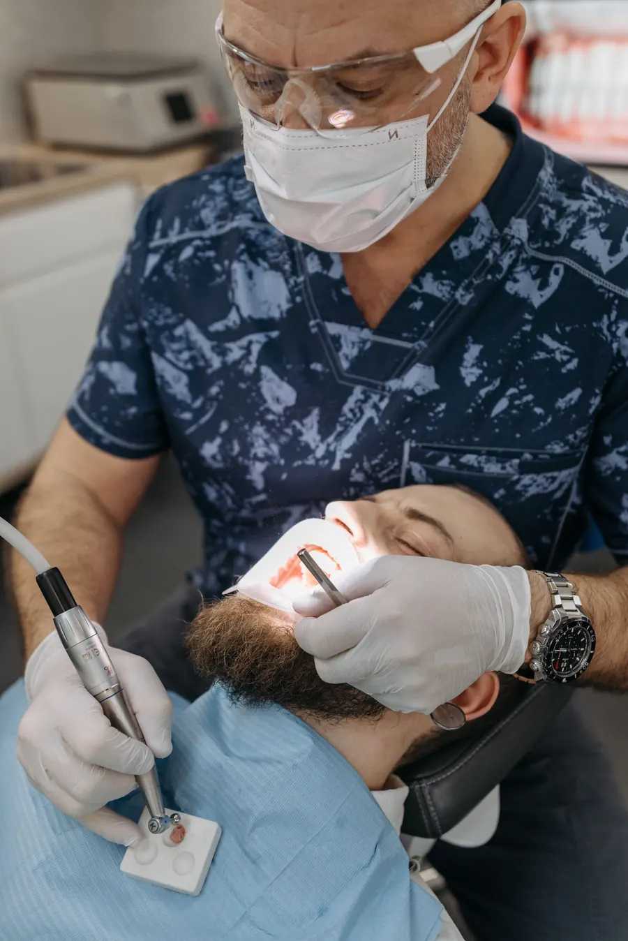 Odontólogo con barbijo y protección ocular trabajando sobre la boca de un paciente